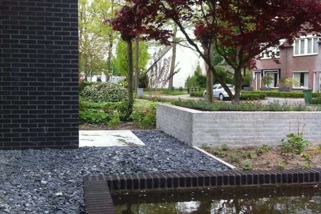 Metselen van een tuinmuur in het water in een achtertuin in Goirle. Deze tuin is ontworpen door Antoon van Spelde