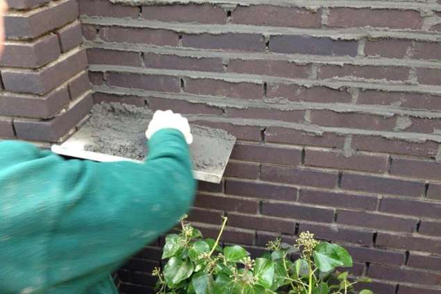 voegen van een strakke zwarte tuinmuur. hoe een tuinmuur metselen in de tuin.