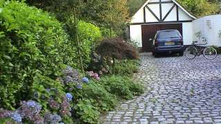 oprit van kinderkoppen met blauwe hortensia laurierhaag en vaste planten