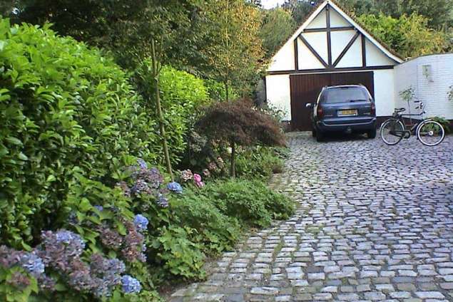 oprit van kinderkoppen met blauwe hortensia laurierhaag en vaste planten